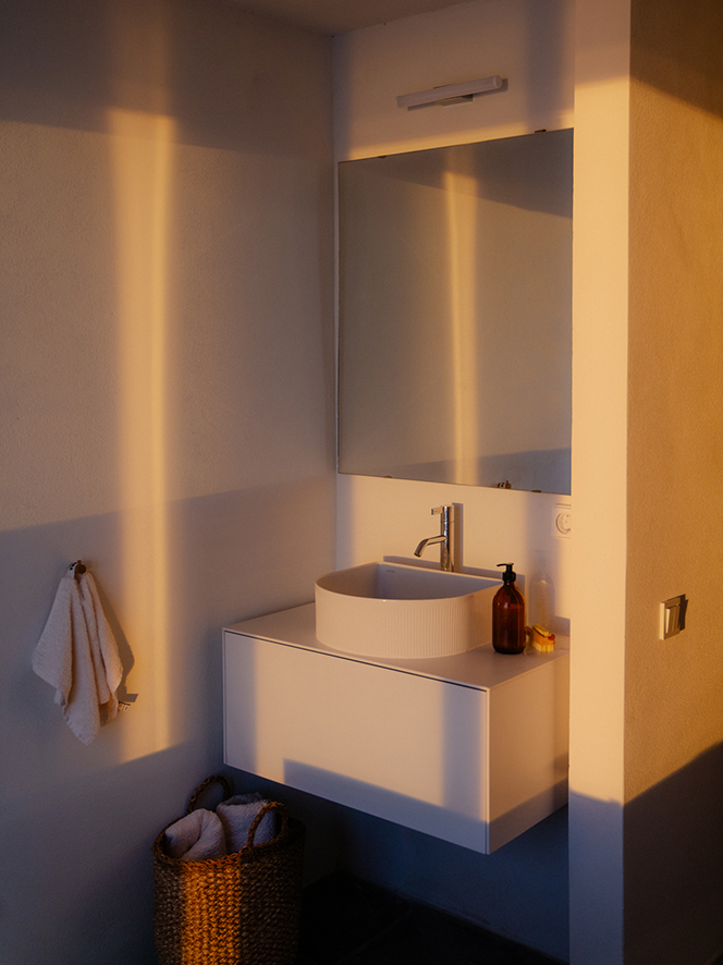 Weiße keramische Waschtischschale mit Armatur, weißes Waschtisch-Unterschrank, Spiegel an der Wand mit Beleuchtung