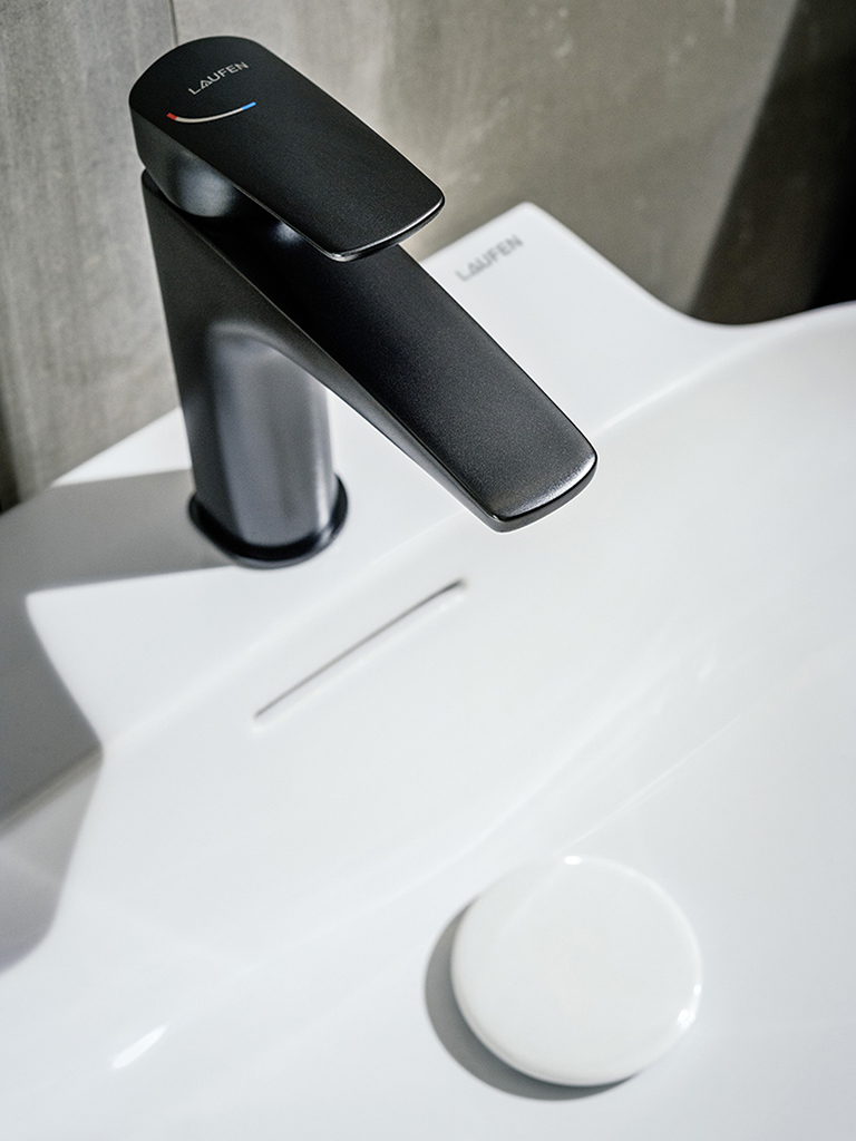 Schwarze Armatur auf weißem Waschtisch vor grauem Hintergrund