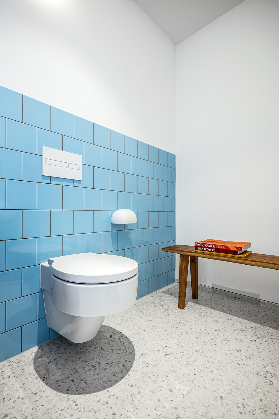 Weißes Hänge-WC und Drückerplatte auf blauen Fliesen und Holz Sitzbank