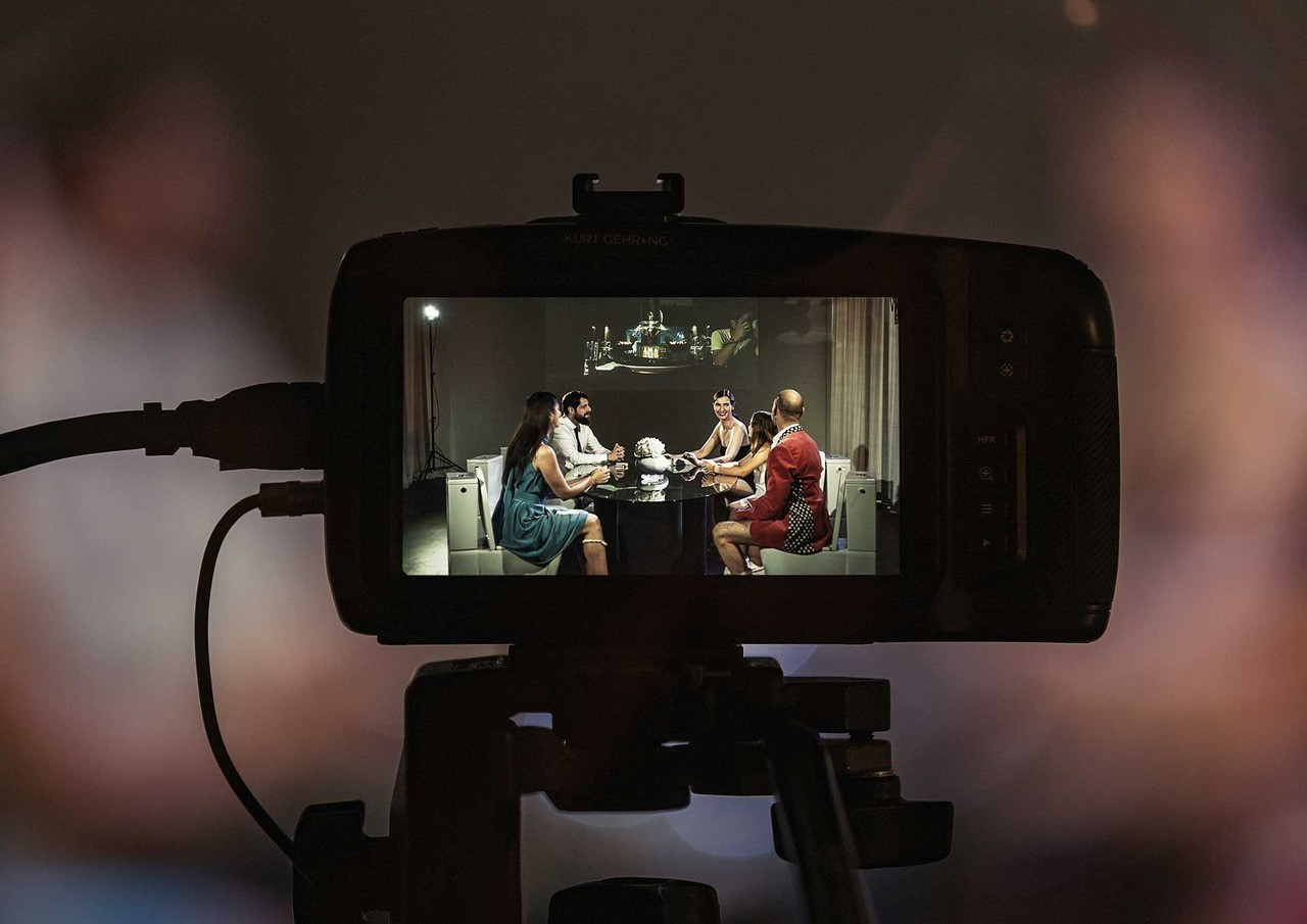 Bild von Display einer Kamera, mit vier Menschen die beim Tisch sitzen und sich unterhalten