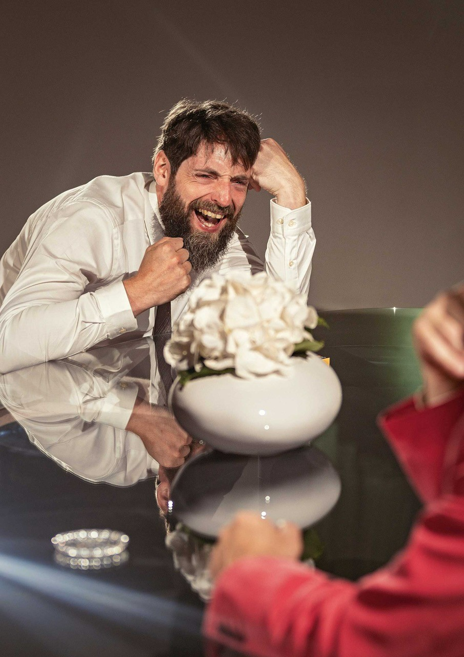 Mann in weißem Hemd sitzt bei einem Glasstisch und lacht