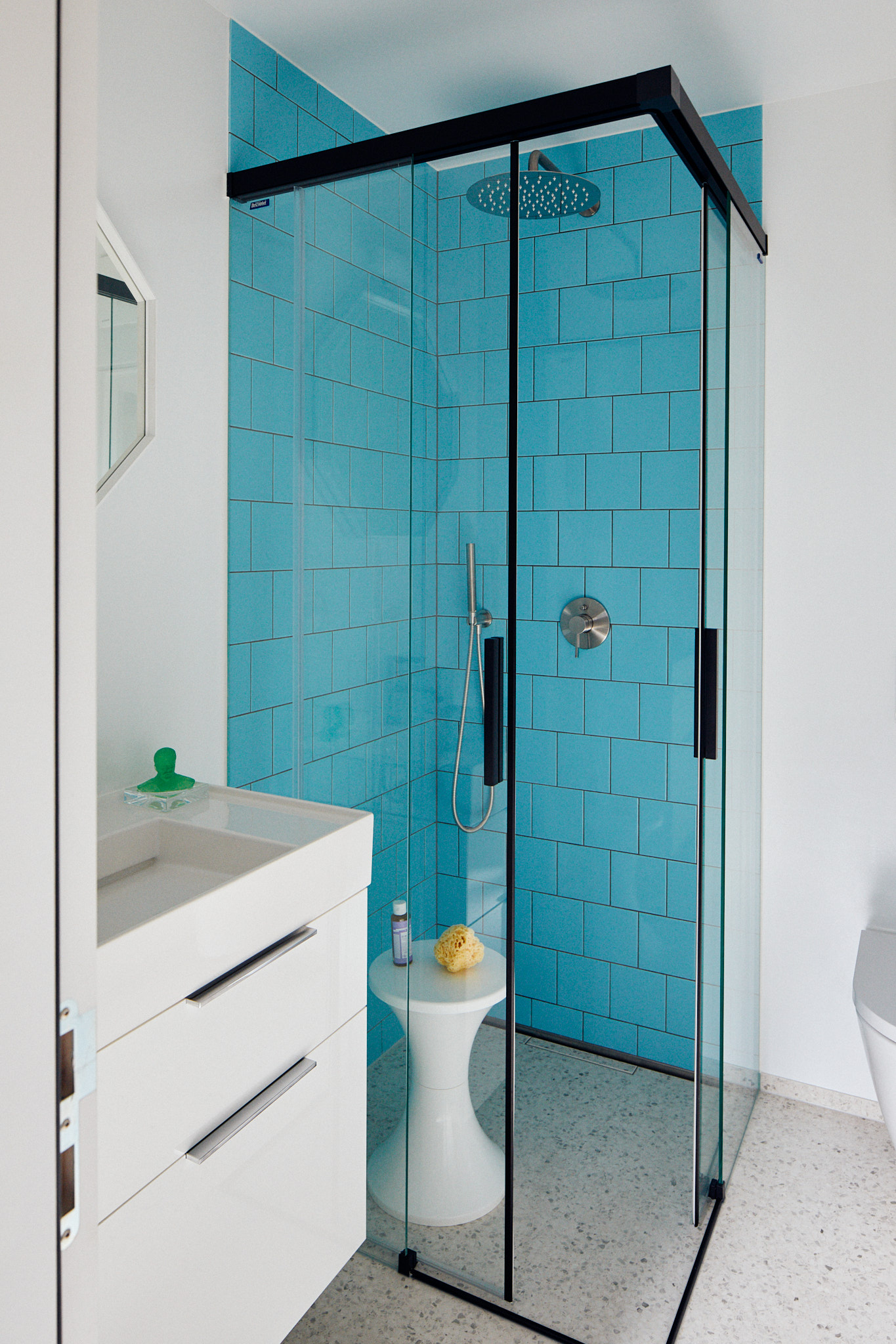 Weißer Waschtisch mit weißem Waschtisch Unterschrank und oktogonalem Spiegel, Duschwannen mit Abtrennung und blauen Fliesen