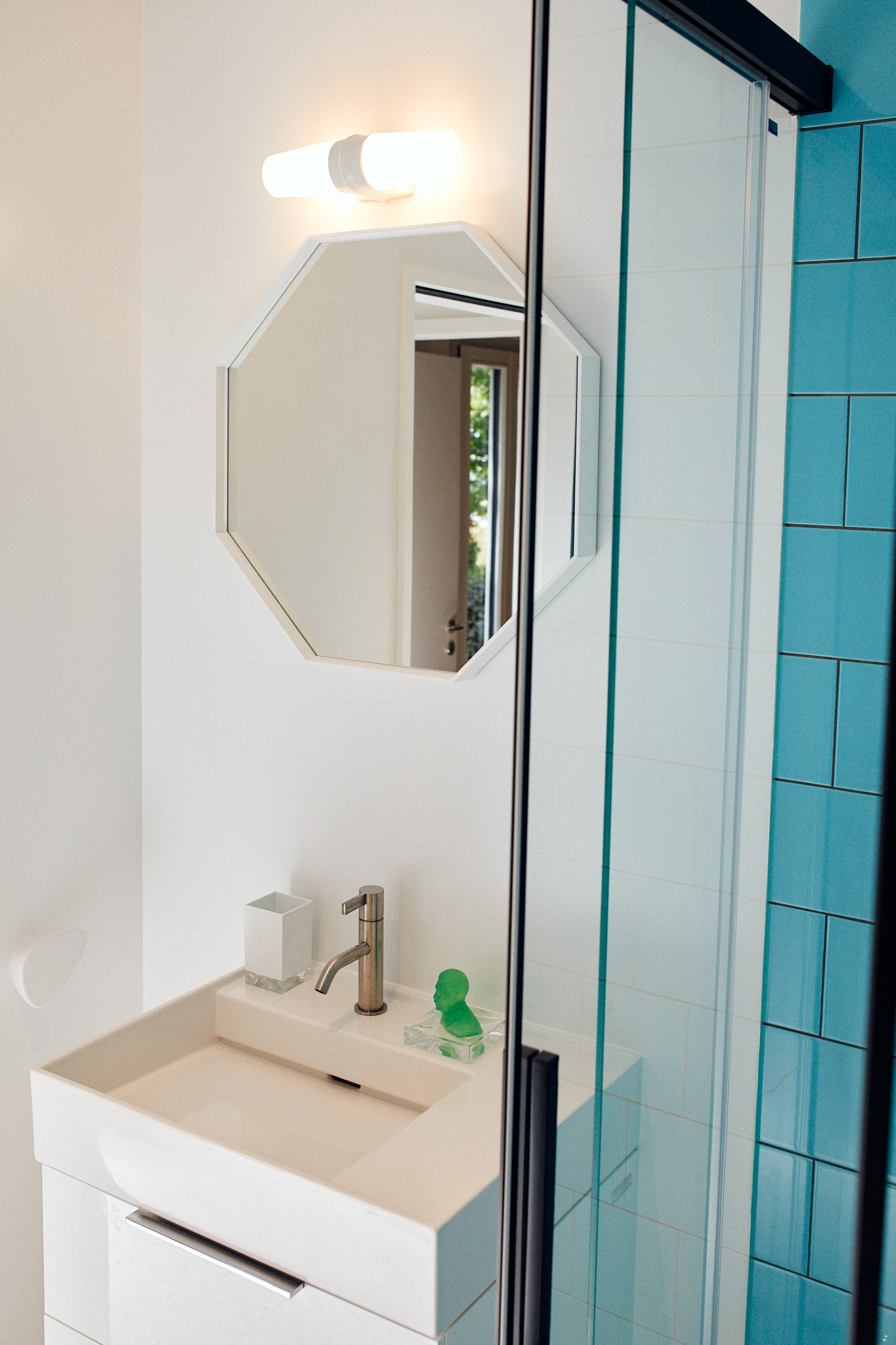Weißer Waschtisch mit weißem Waschtisch Unterschrank und oktogonalem Spiegel, Duschwannen ABtrennung und blauen Fliesen
