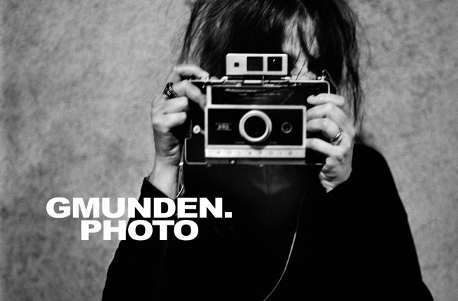 Schwarz-weißes Foto einer Frau mit alter Kamera vor dem Gesicht und Überschrift Gmunden.Photo