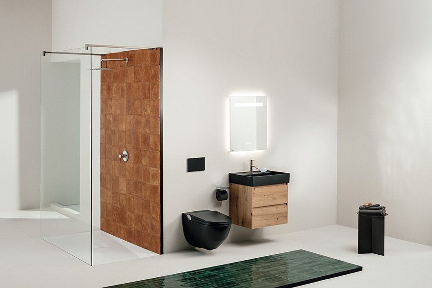 Badezimmer mit schwarzer Keramik (Dusch-WC, Waschtisch), Holzmöbel, Dusche mit kupfer-farbenen Fliesen an der Wand, im Vordergrung grüne Bodenfliesen