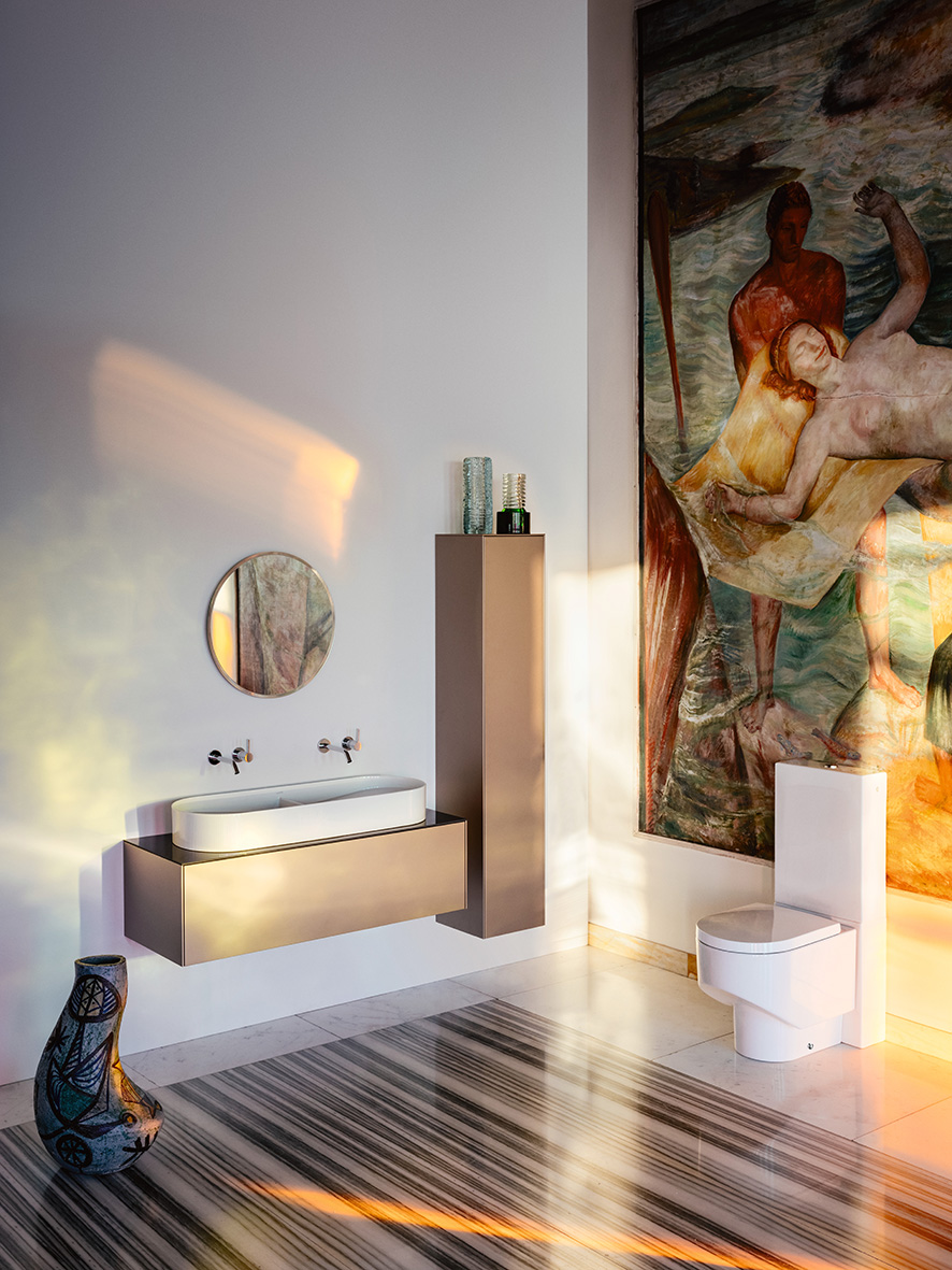 Badezimmer mit weißem Waschtisch auf kupfer farbenem Möbel, mit kupfer-farbenem Hochschrank, weißes Stand-WC vor bunt bemalter Wand