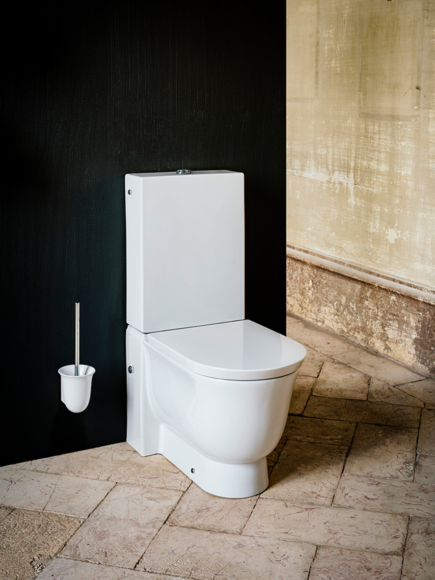 Weißes Stand WC vor dunkler Wand, mit Toiletten Bürsten-Halter, gefliester Boden