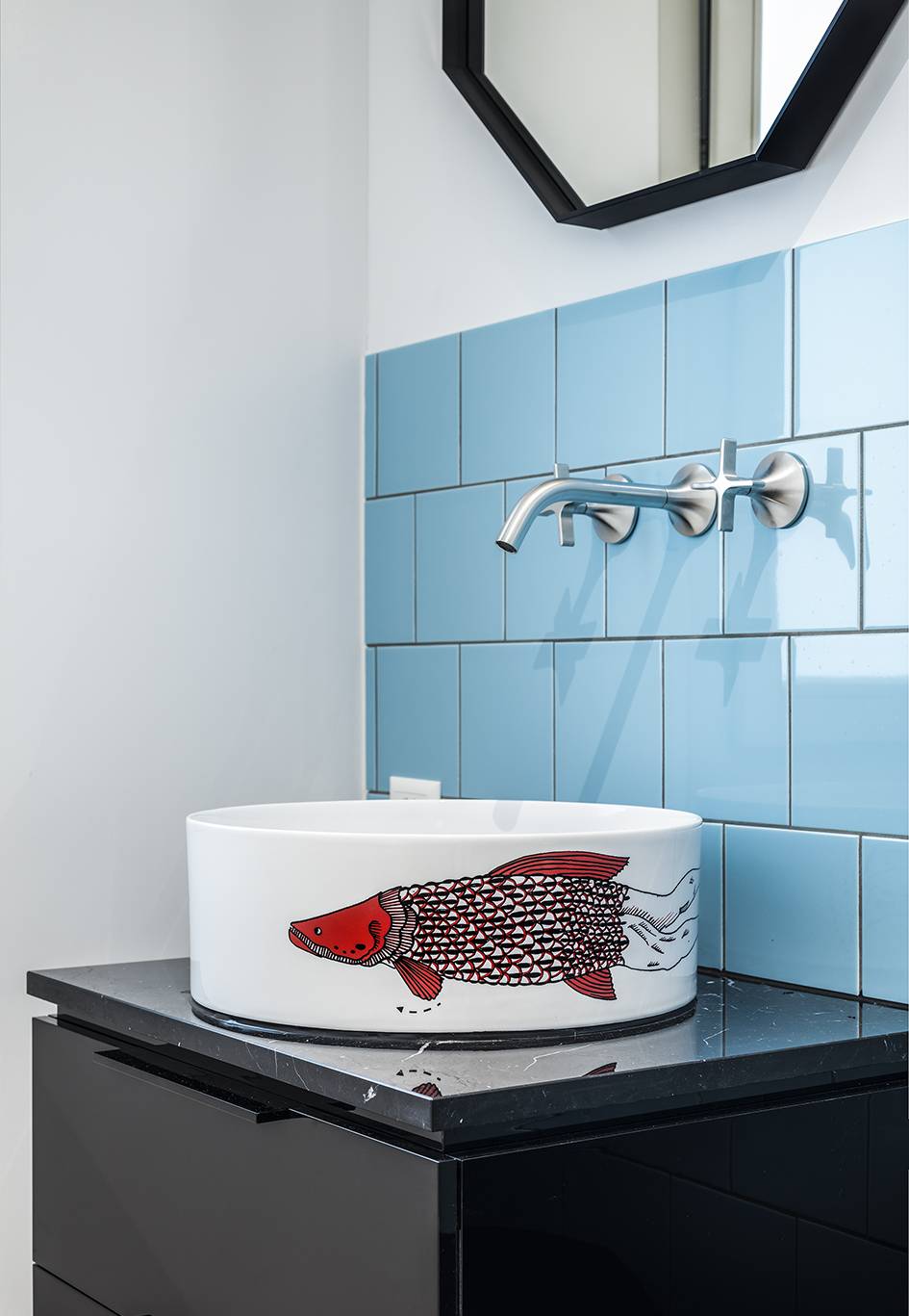 Waschtisch-Schale mit rotem Fish-Muster, auf dunkel-braunem Unterschrank mit Wandarmaturen auf blauen Fliesen und Spiegel mit schwarzem Rahmen