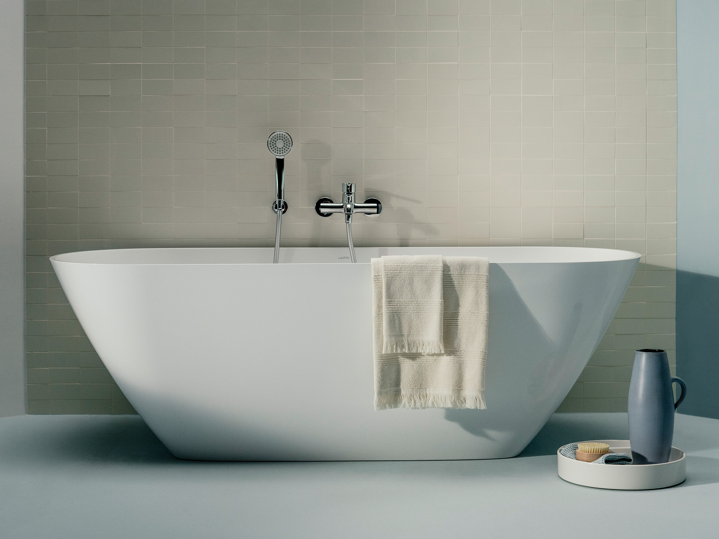 Freistehende Badewanne vor gefliester beige-farbener Wand, Badezimmer Dekoration und Handtuch