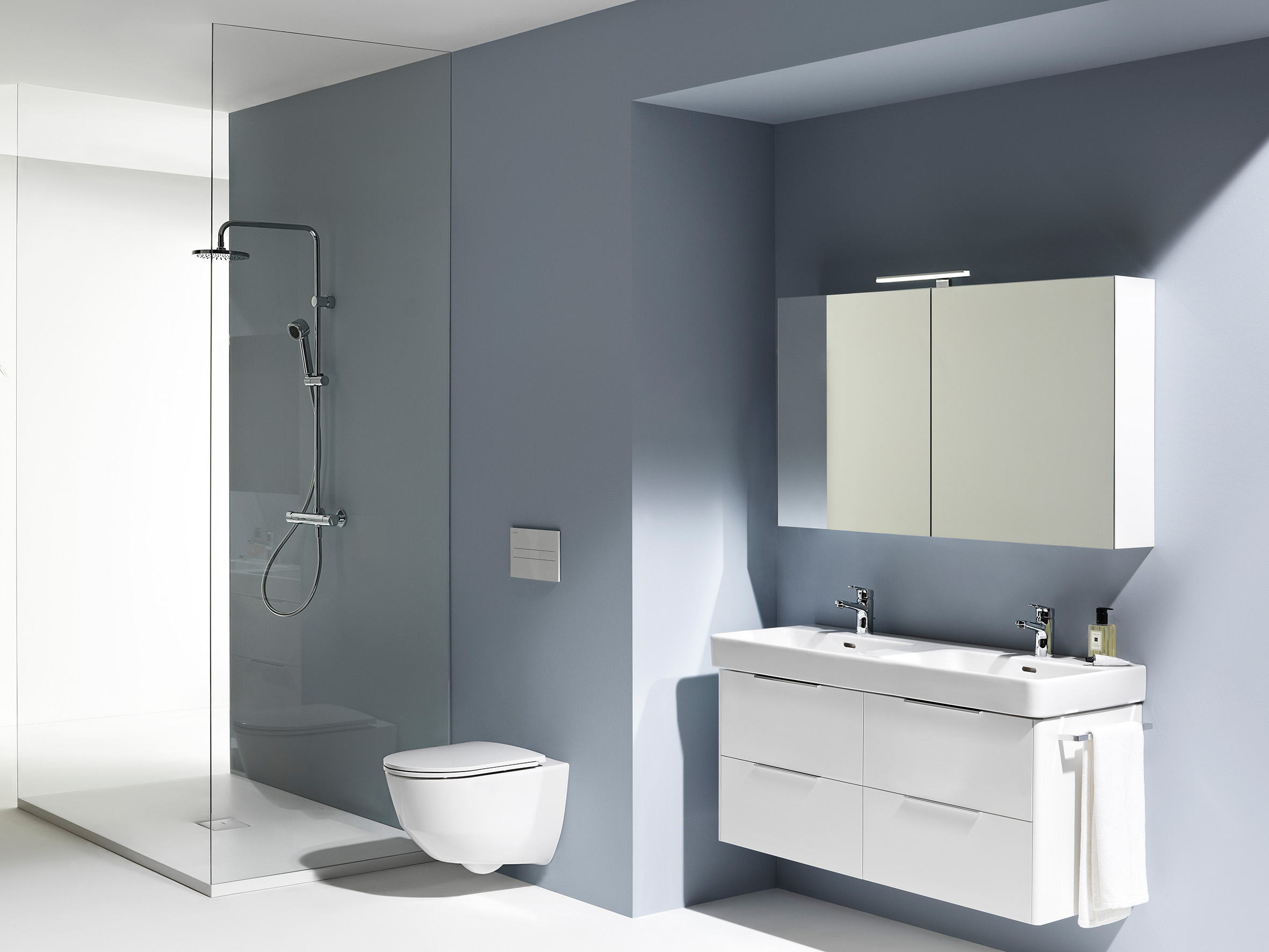 Cleanes Badezimmer-Scene mit sanft blauer Wand, weißer Doppel-Waschtisch mit Unterschrank, Spiegelschrank, WC und Dusche 
