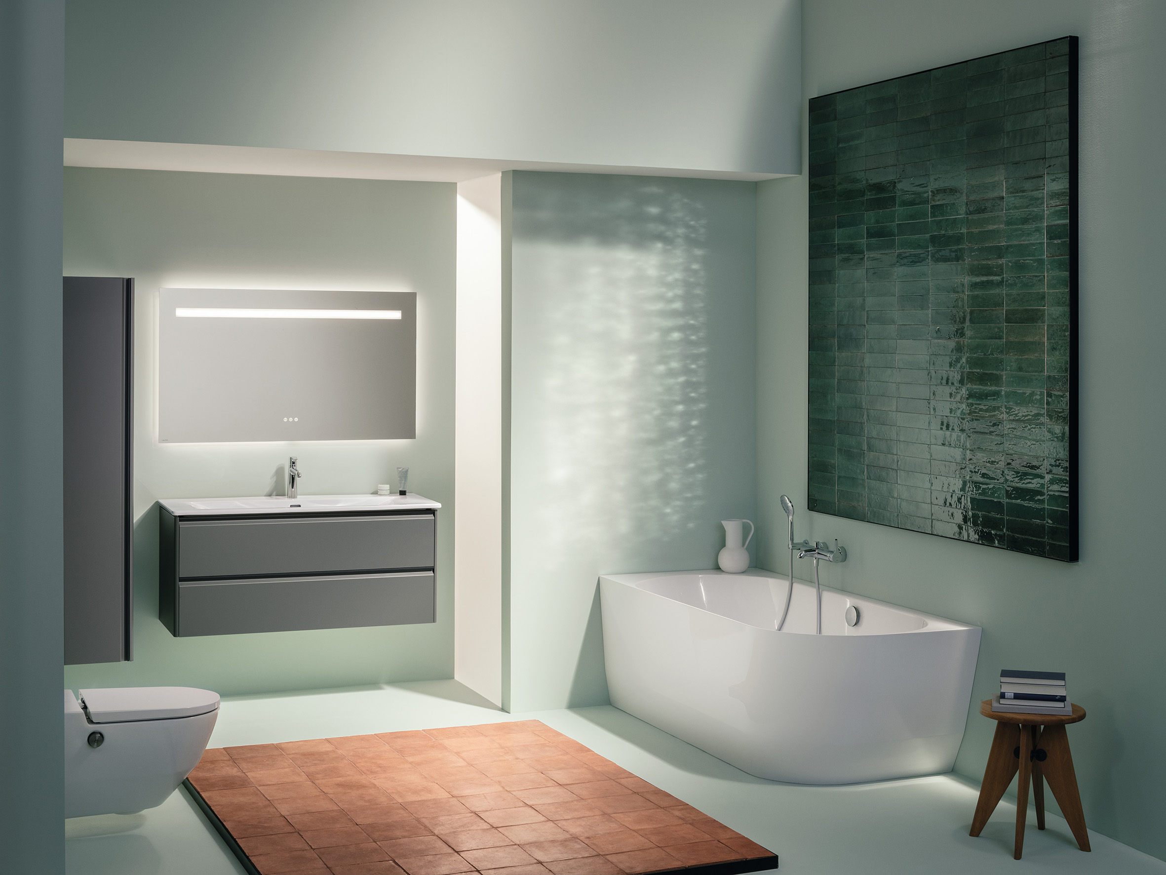 Badezimmer Scene mit sanft-grünen Wänden, weißer Eckbadewanne, weißem WC und Waschtisch-Set, bestehend aus weißem dünnem Waschtisch, grauem Möbel und Spiegel